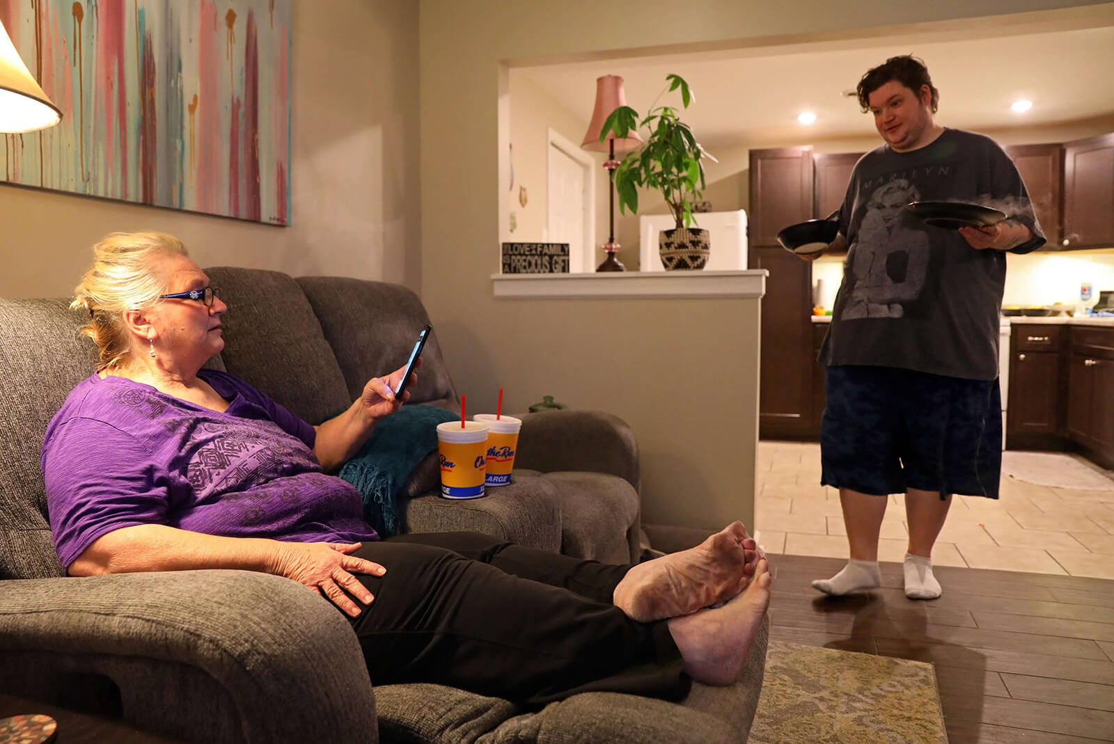 Dan Schicker brings a plate of food to his mother, Lonni Schicker, before they share a meal together on the couch in their Fenton apartment on Monday, July 30, 2018. The two, as roommates, spend a lot of their time at home watching television. Lonni, who was diagnosed with dementia in April, now is having problems operating the remote control and her phone.