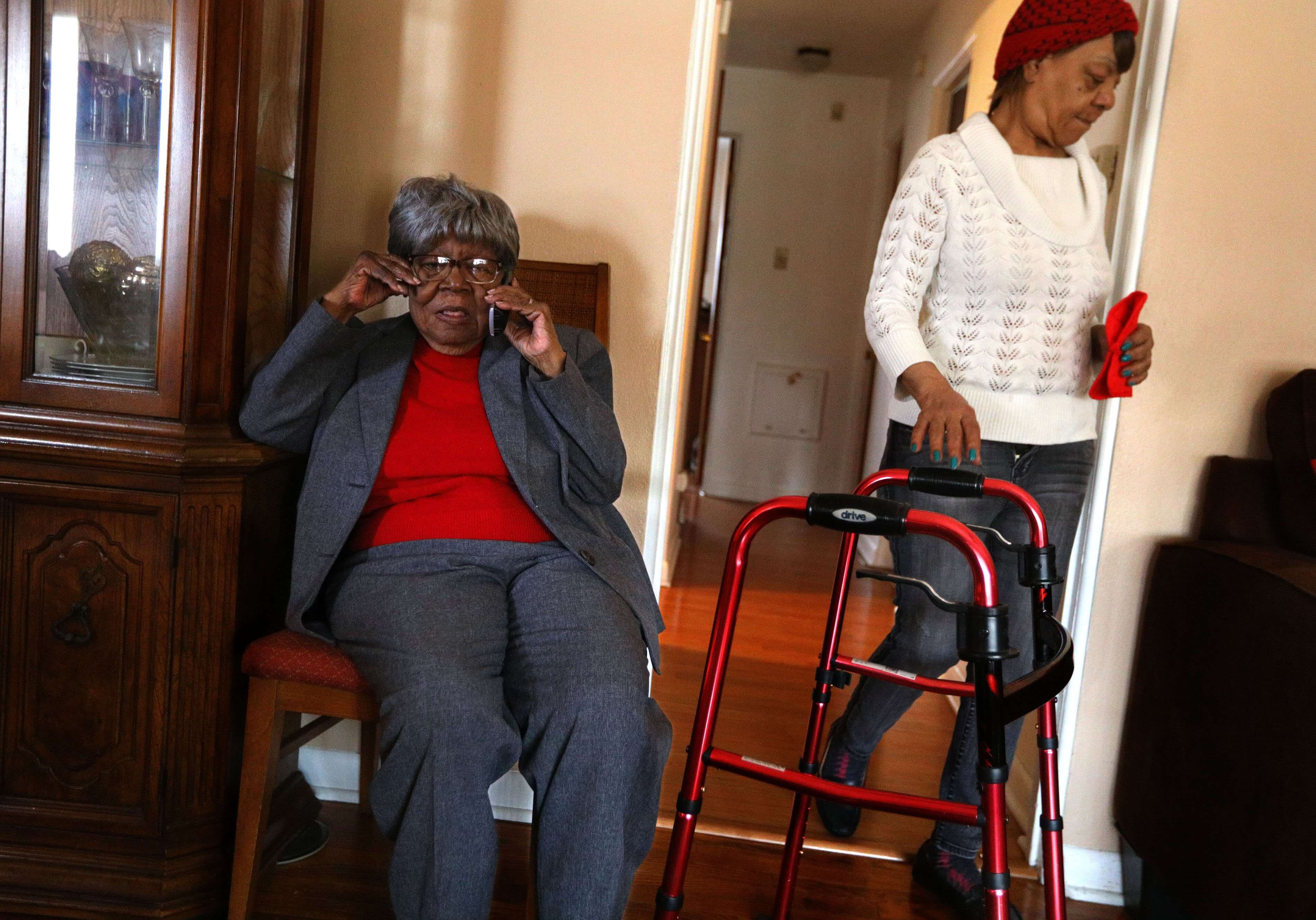 Barbara Lewis, (left), talks on the phone with her son on Wednesday, Dec. 19, 2018, as her daughter, Rosalyn Stiles, (right), dodges a walker in the doorway in their University City home. Lewis' memory problems began four years ago. She found the sermons at her church confusing, left ingredients out of her pies and cakes, and thought people were moving her things.